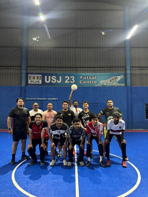 The SNT futsal side lined up on a blue indoor court, one player holding the ball above his head.