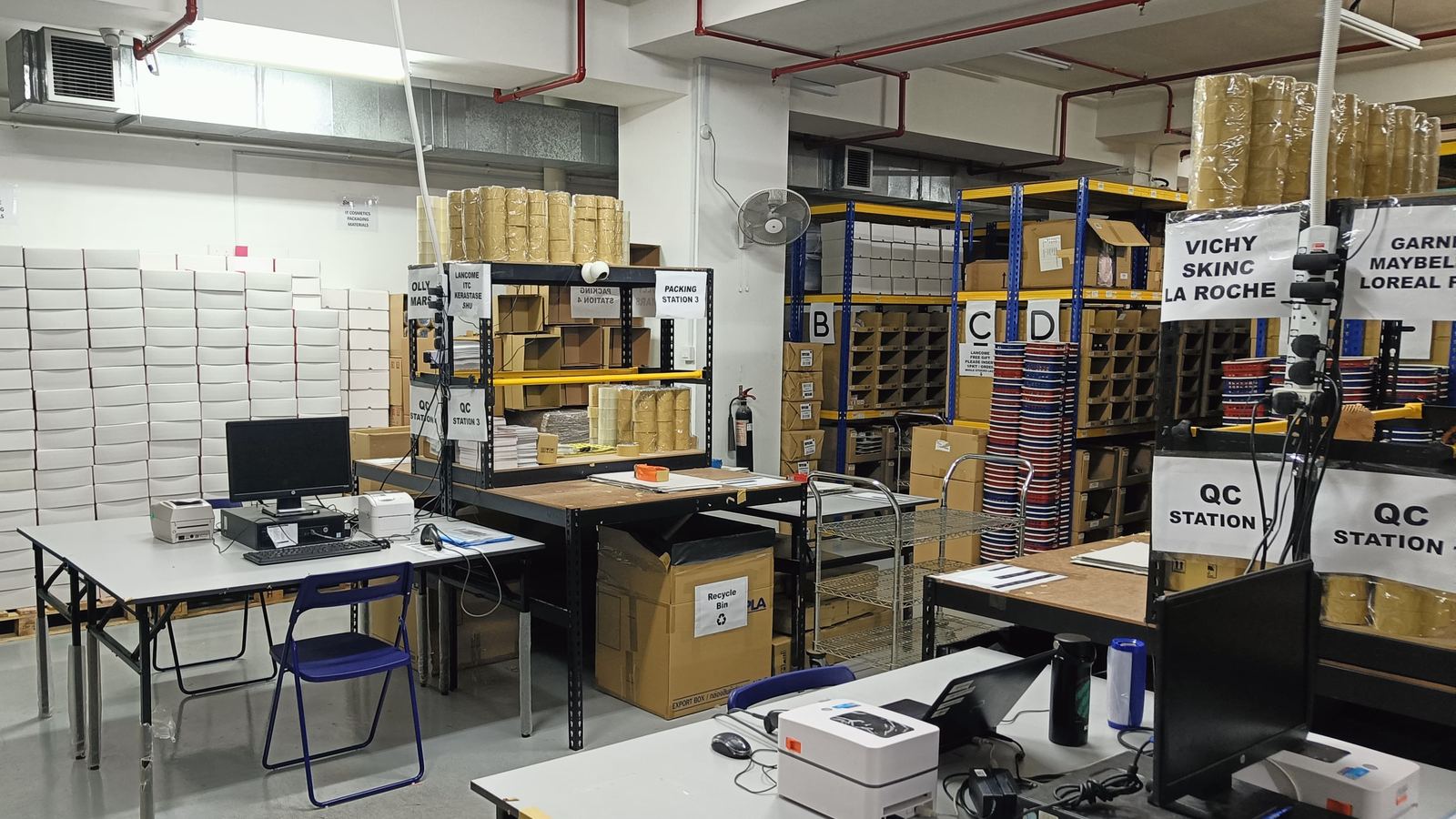 Quality-control benches in the Singapore centre, screens and label printers on the tables under QC station signs.