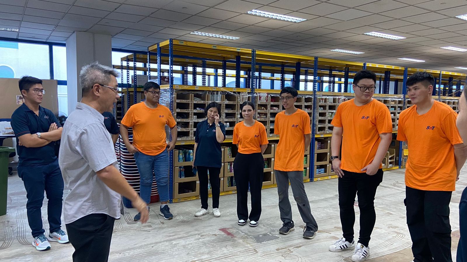 Operators in SNT shirts standing on the Singapore floor with a supervisor, racking running away behind them.