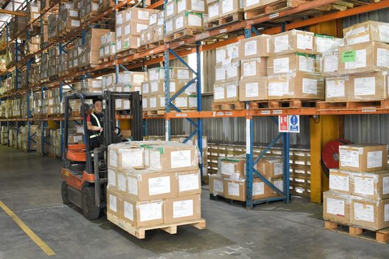 A forklift setting down a wrapped pallet in front of racking stacked several levels high.