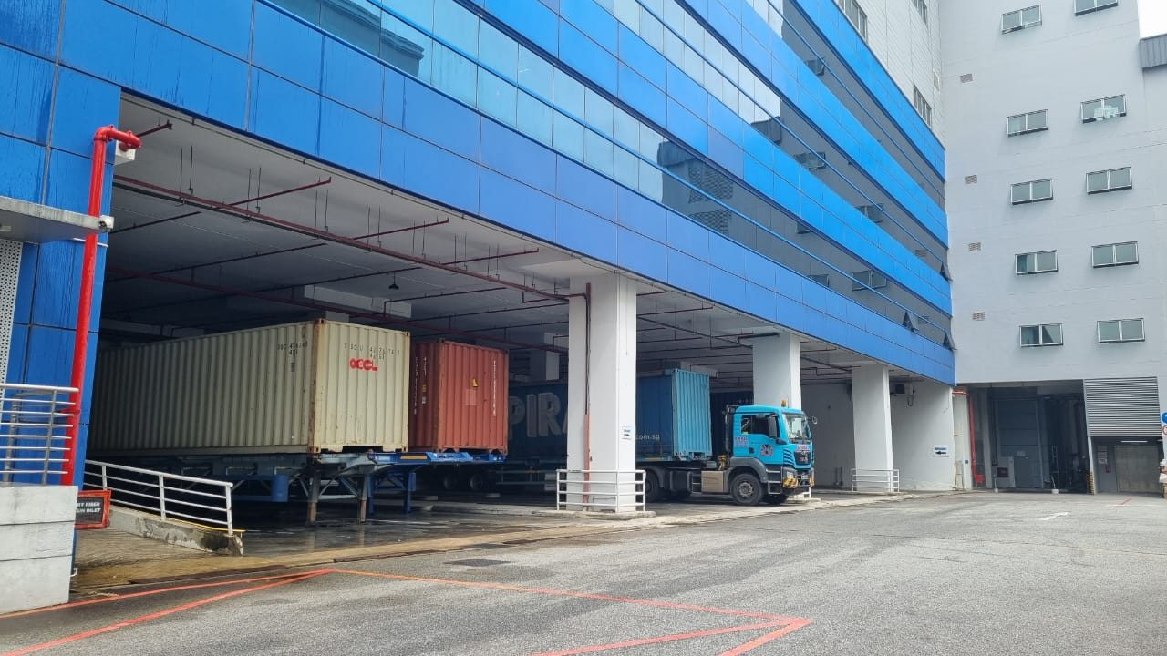 The loading bays beneath 10 Changi South Street 2, containers backed in under the building and a prime mover waiting on the apron.
