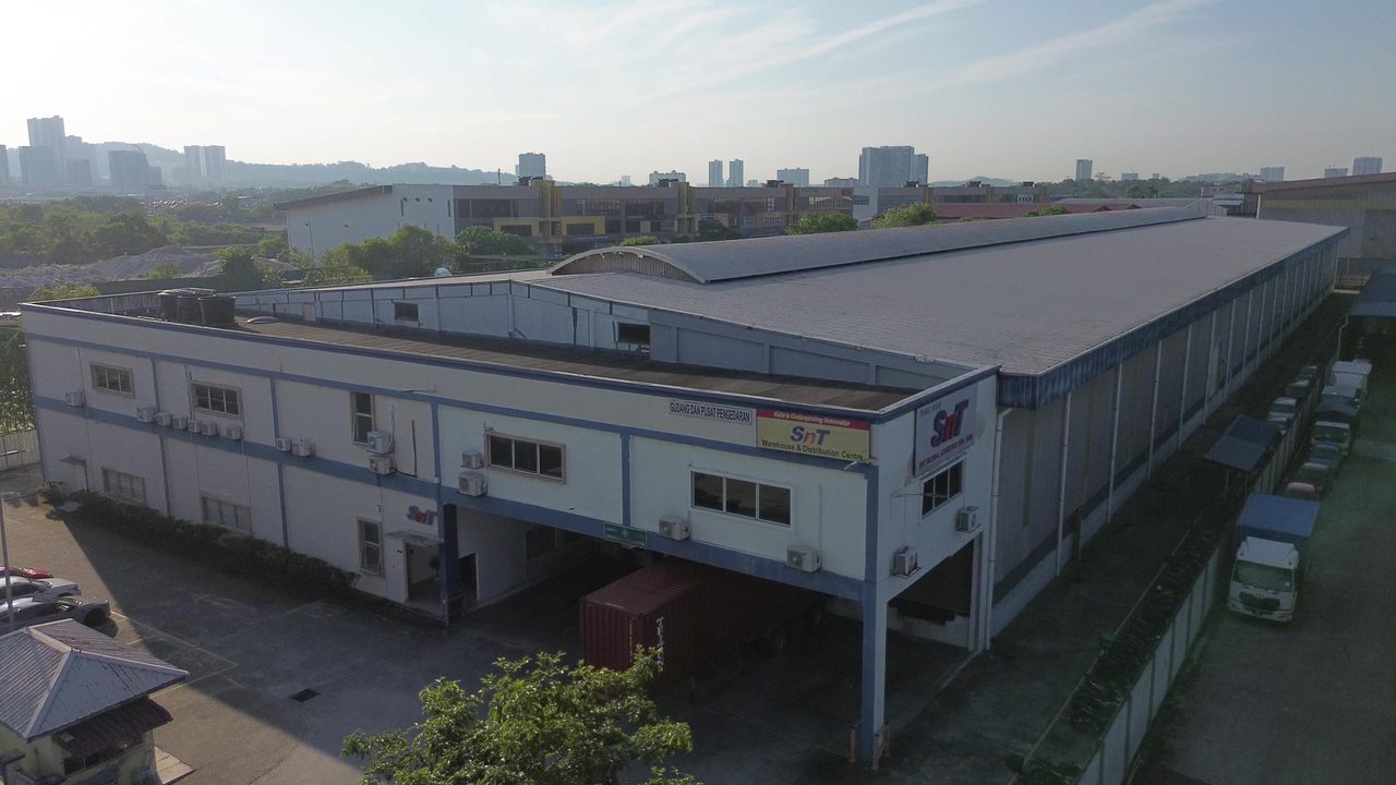 The Subang Jaya headquarters from the air, the SNT sign along the upper floor and a container standing at the dock below.