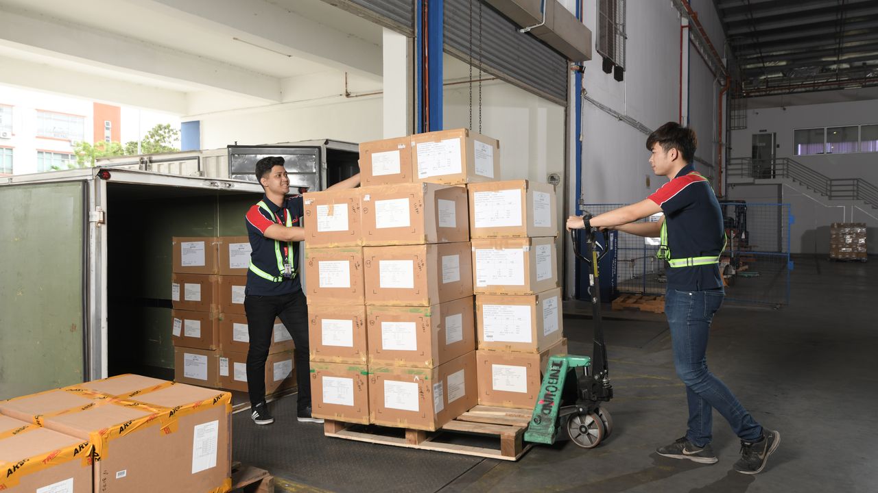 Two operators moving a pallet of cartons into a container at the Subang Jaya II dock, one steering the pallet jack and the other steadying the stack at the trailer door.